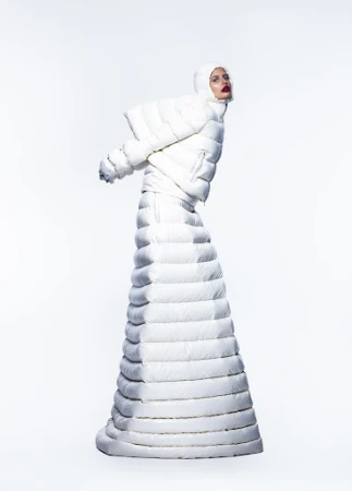 Model wearing a matching white padded puffer jacket and long quilted skirt with a hooded headpiece against a plain white studio background.