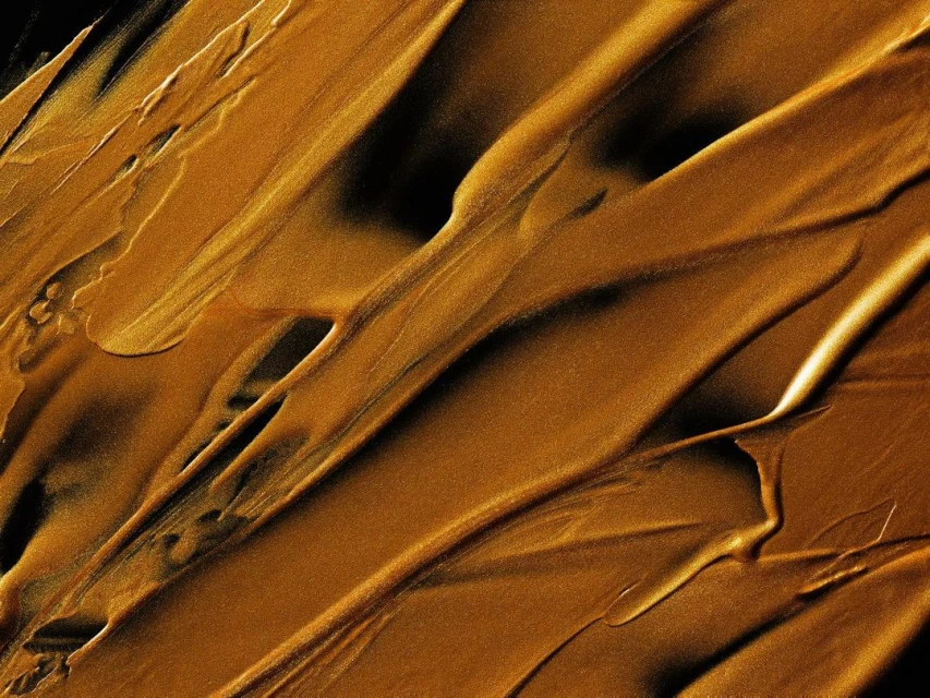 Abstract close-up of golden liquid or paint texture, featuring diagonal smudges, rich color variations, and dark shadows, ideal for backgrounds.