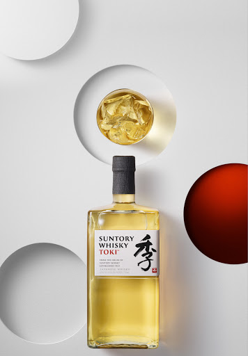 Suntory Whisky Toki bottle and whisky glass with ice, set against white circular background for a clean, minimalist aesthetic.