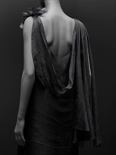 Monochrome shot of a mannequin displaying an elegant dress with a shoulder floral accent, in a minimalist, dark setting.