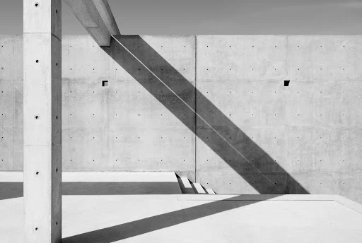 Architectural abstract featuring concrete structures with strong geometric lines and deep shadows against a clear sky.