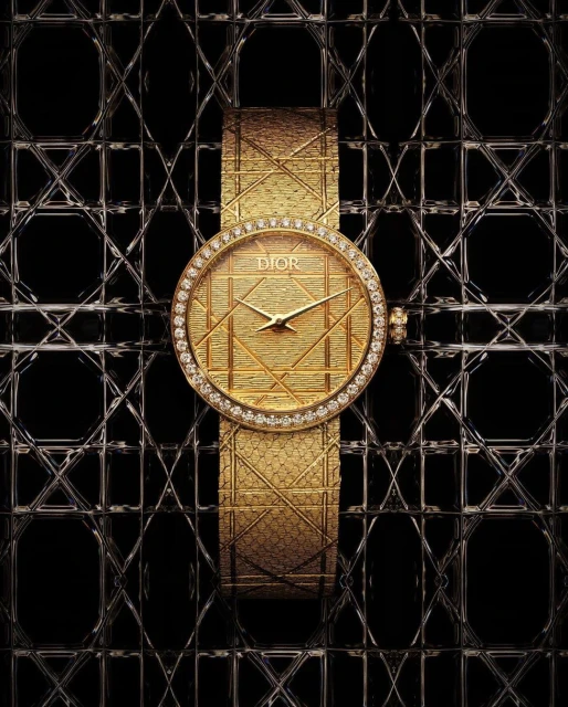 Elevated, eye-level studio shot showcases a gold Dior watch featuring a diamond bezel and a patterned dial on a black patterned surface.