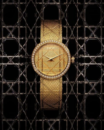 Elevated, eye-level studio shot showcases a gold Dior watch featuring a diamond bezel and a patterned dial on a black patterned surface.