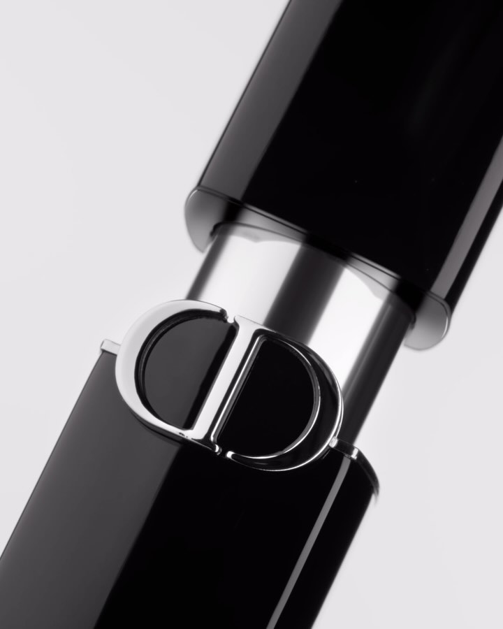 Extreme close up of a black and silver lipstick tube featuring the prominent Christian Dior CD logo against white