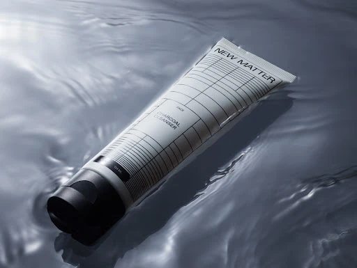 Product shot of a New Matter charcoal cleanser tube floating in rippling water, showcasing its sleek design and skincare application.