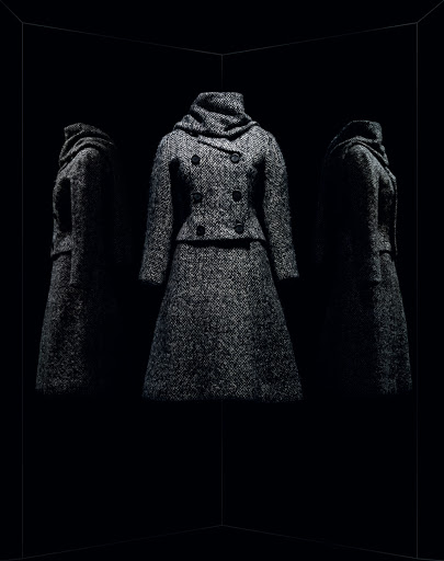 Elegant wool coat and skirt ensemble is spotlighted against a stark black background with mirrored reflections, showcasing fabric texture.