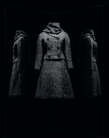 Elegant wool coat and skirt ensemble is spotlighted against a stark black background with mirrored reflections, showcasing fabric texture.