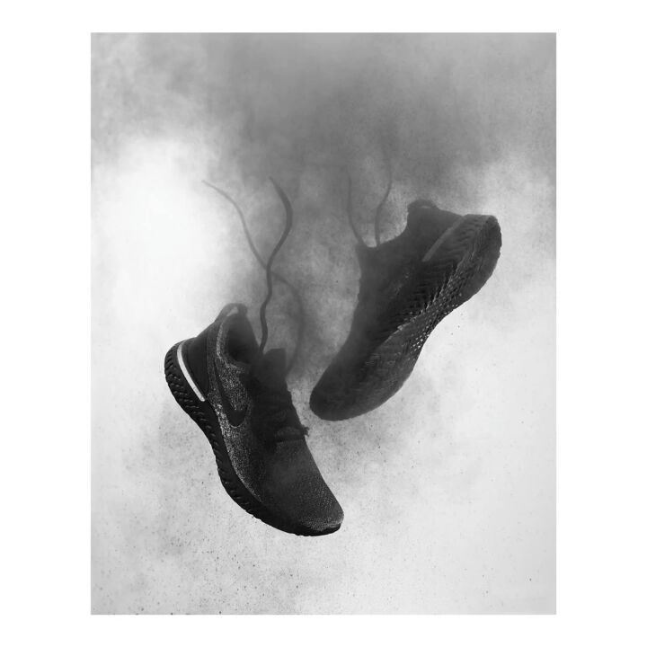 Two black athletic running shoes floating in a monochrome studio shot with a gray dusty background.