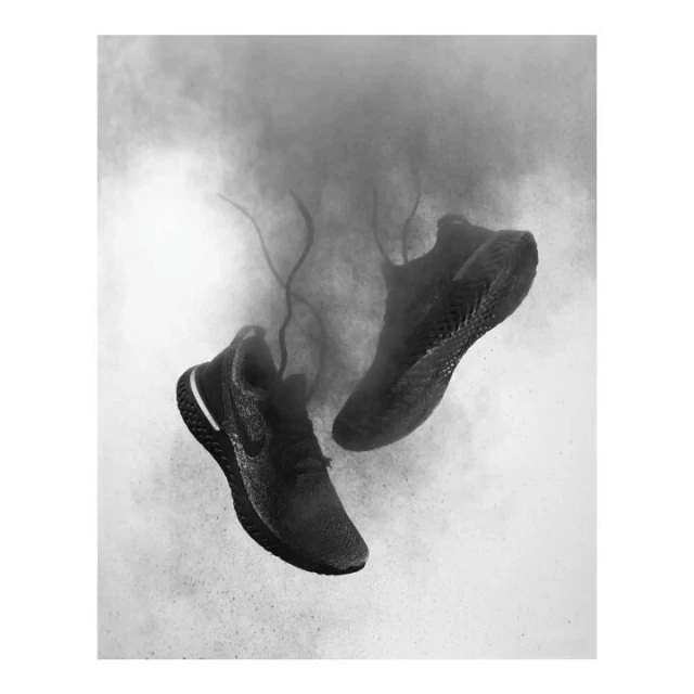 Two black athletic running shoes floating in a monochrome studio shot with a gray dusty background.