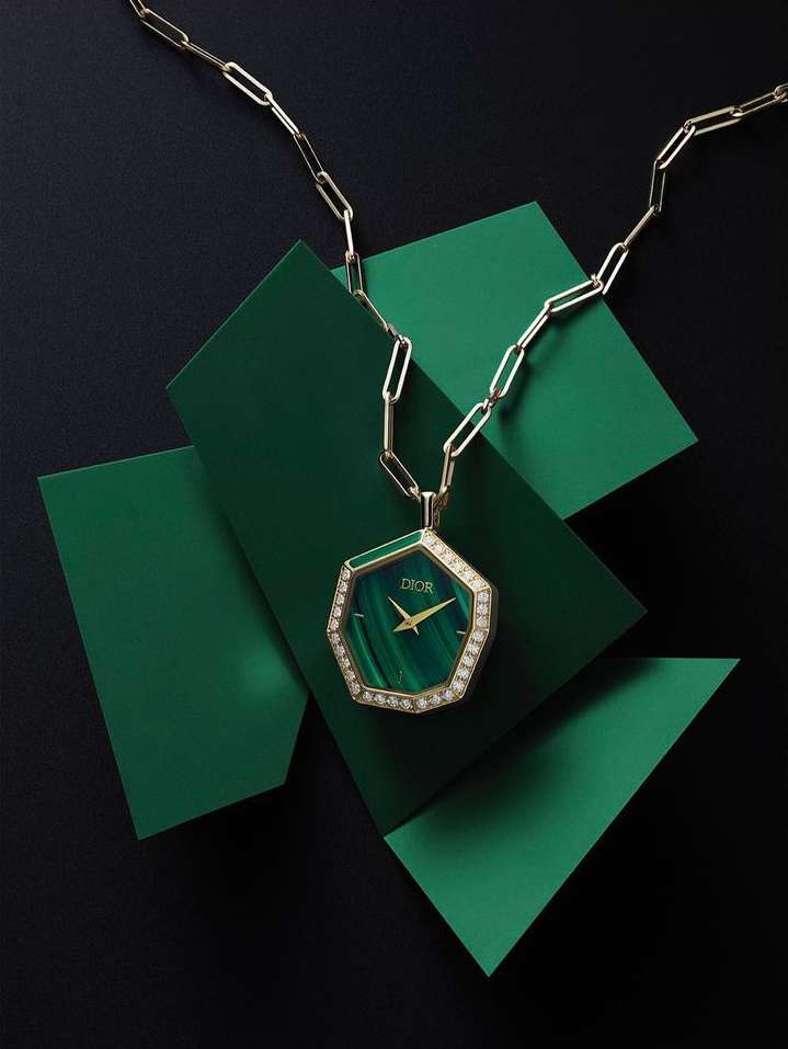 Elegant gold chain necklace with Dior watch pendant on green geometric platforms over black. Jewelry design and product shot.