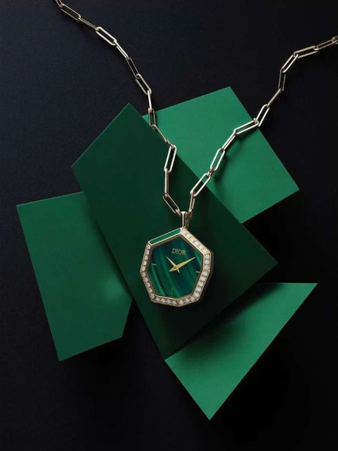 Elegant gold chain necklace with Dior watch pendant on green geometric platforms over black. Jewelry design and product shot.