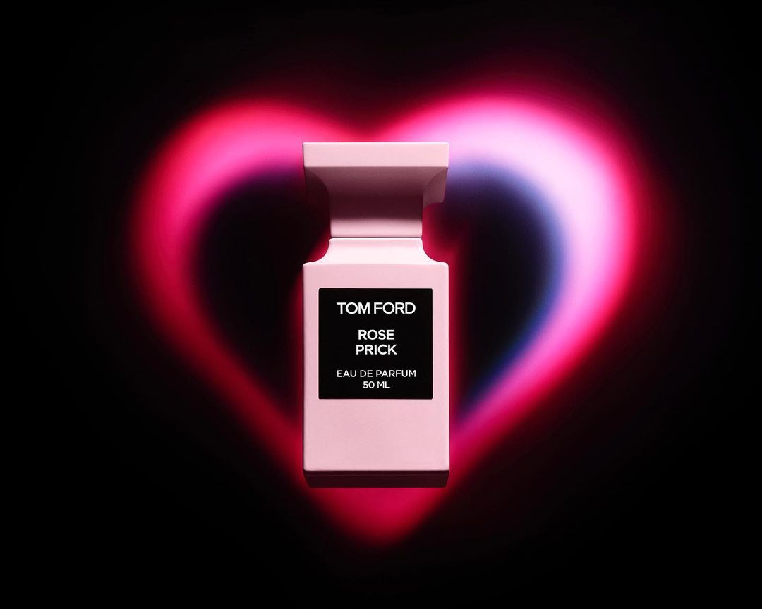 Tom Ford Rose Prick perfume bottle in light pink color against a black background with a blurred pink heart shape.