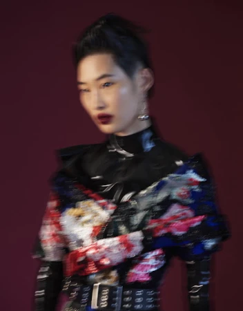 Motion blurred portrait of an East Asian woman wearing a dark patterned top and dark lipstick against a deep red background.