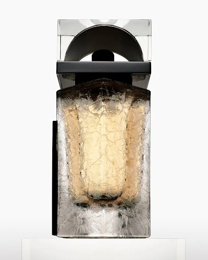 Elegant fragrance bottle with a geometric cap, showcasing a frosted texture and amber hue against a bright backdrop.