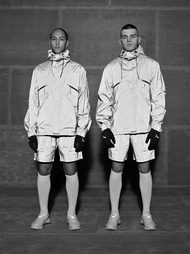 Two adult males pose in reflective athleisure wear against a textured grey background, showcasing modern sportswear and fashion.