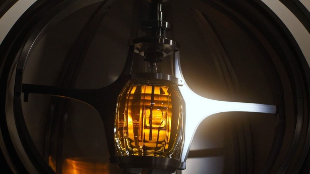 Close-up of a glass distilling apparatus with a golden liquid inside, set against a backdrop of industrial metal and dark tones.