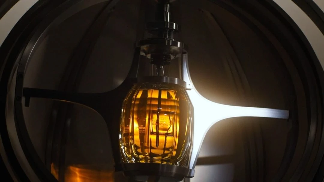 Close-up of a glass distilling apparatus with a golden liquid inside, set against a backdrop of industrial metal and dark tones.