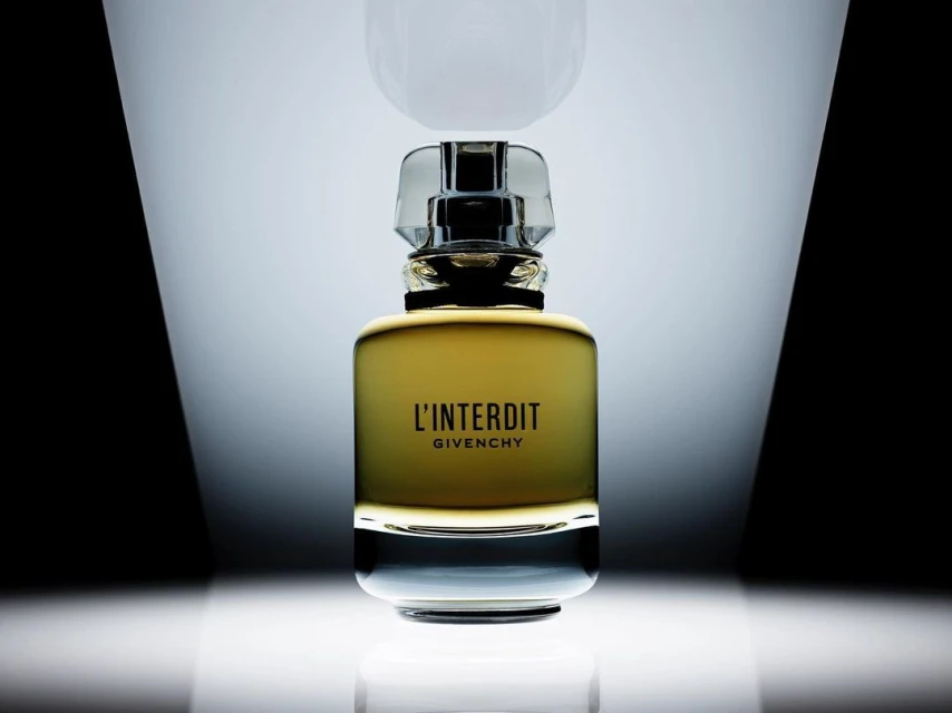 Close-up of a glass bottle of Givenchy L'Interdit perfume with a clear stopper against a black-and-white gradient background.