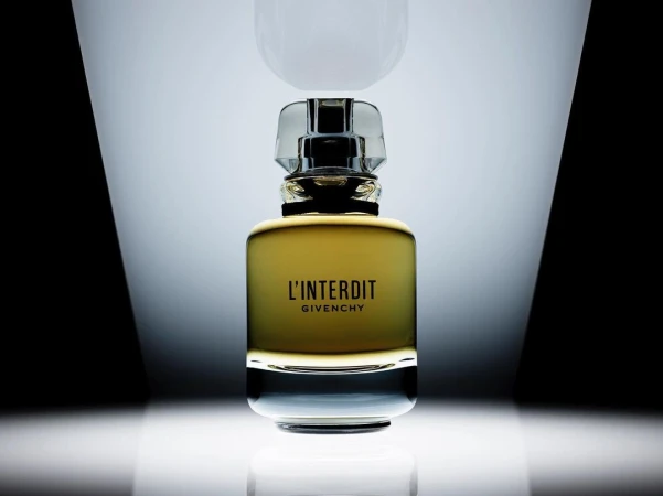 Close-up of a glass bottle of Givenchy L'Interdit perfume with a clear stopper against a black-and-white gradient background.