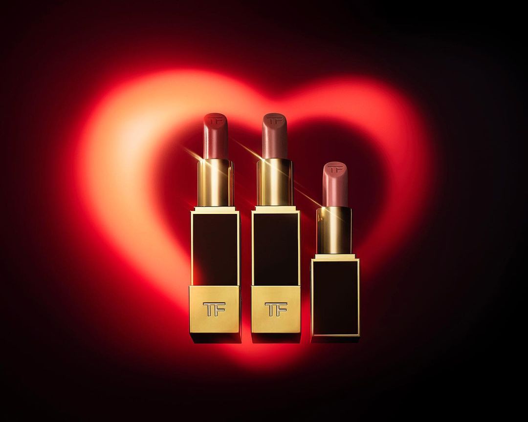 Three Tom Ford lipsticks in a row against a dark background with a red heart-shaped light, beauty and cosmetics.