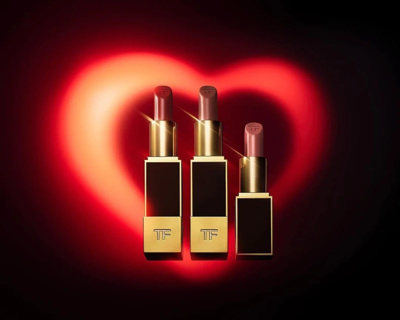 Three Tom Ford lipsticks in a row against a dark background with a red heart-shaped light, beauty and cosmetics.