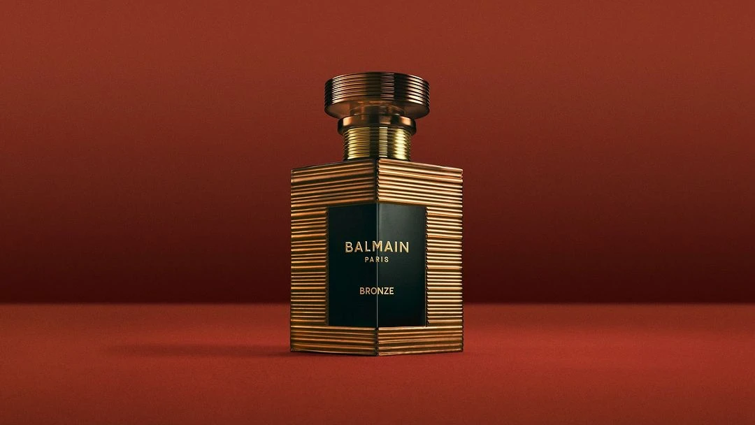 Balmain Bronze perfume bottle on a red gradient background, close-up studio shot for beauty, fashion, and celebrity product marketing.