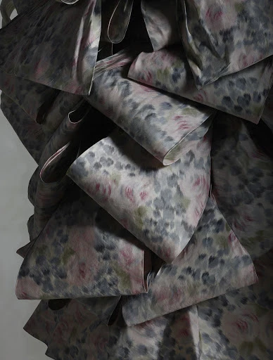 Close-up of a ruffled fabric with a delicate floral pattern in shades of gray, pink, and green, creating a soft, textured effect.