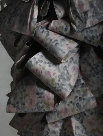 Close-up of a ruffled fabric with a delicate floral pattern in shades of gray, pink, and green, creating a soft, textured effect.