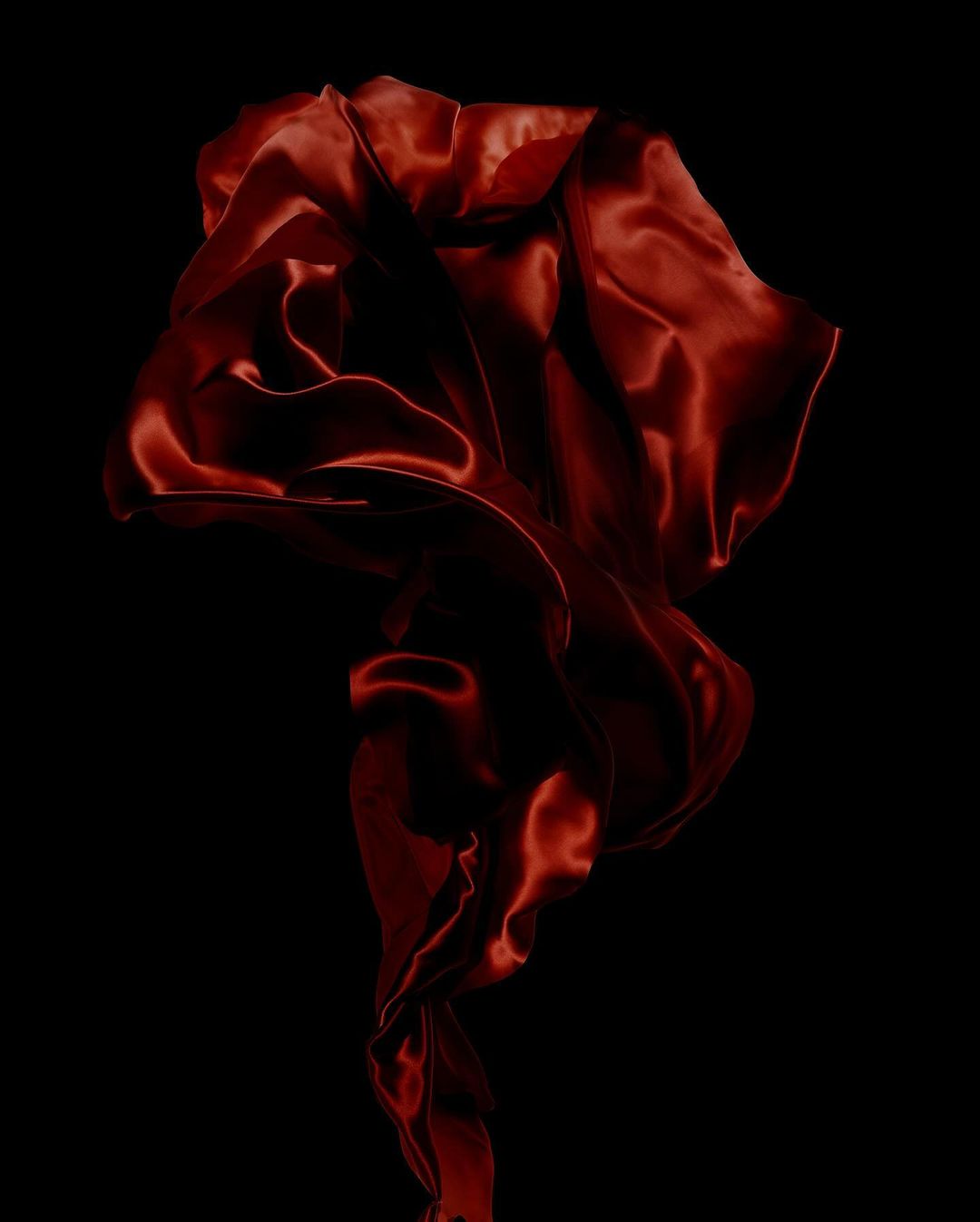Abstract photo of a flowing, draped piece of red satin fabric against a dark background, showcasing the material's texture and movement.