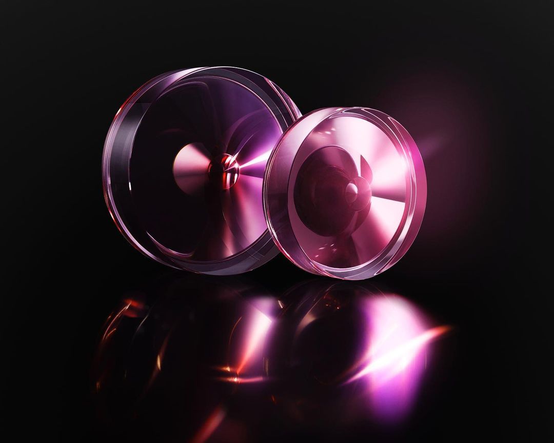 Two transparent, reflective circular objects in shades of purple and pink, set against a dark black background with radiant lighting.