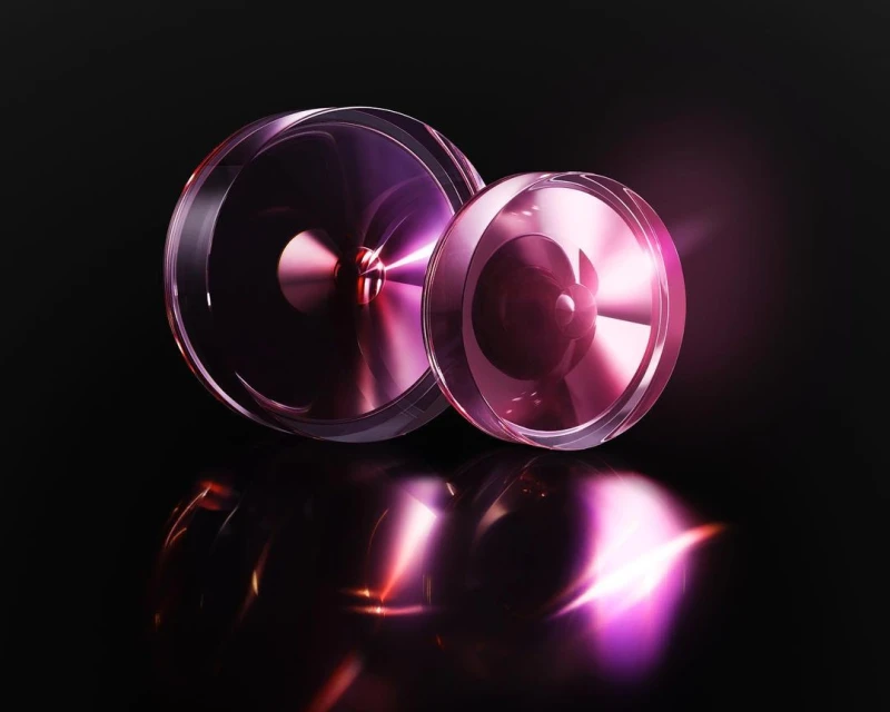 Two transparent, reflective circular objects in shades of purple and pink, set against a dark black background with radiant lighting.