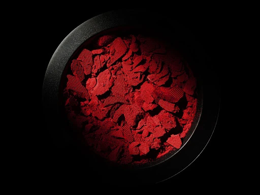 Macro shot of crushed red cosmetic powder in a black container, product photography with studio lighting on a dark background.