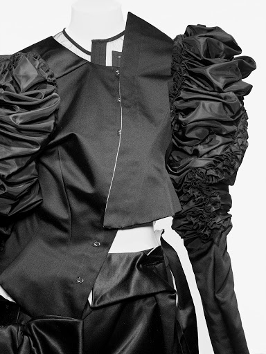 Black and white studio shot of a mannequin dressed in a fashion-forward garment with exaggerated, ruffled sleeves and angular cuts.