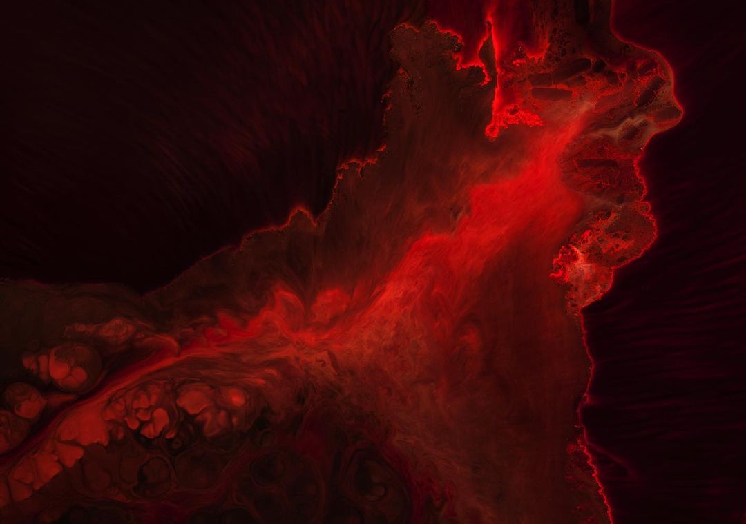 Abstract image featuring dynamic swirling shapes in shades of red against a dark background, resembling smoke or fluid dynamics.