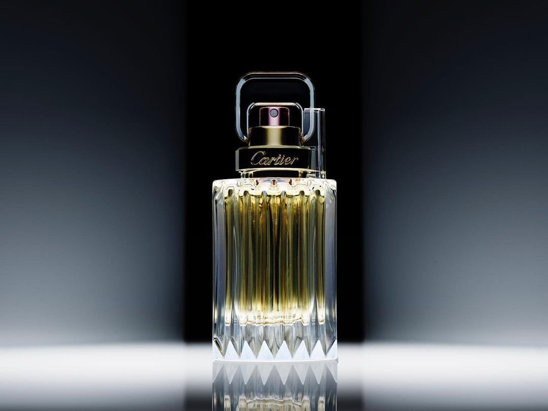Elegant still life of Cartier fragrance bottle with gold accents and faceted glass design on a reflective surface, captured in studio lighting.