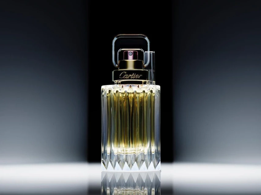 Elegant still life of Cartier fragrance bottle with gold accents and faceted glass design on a reflective surface, captured in studio lighting.