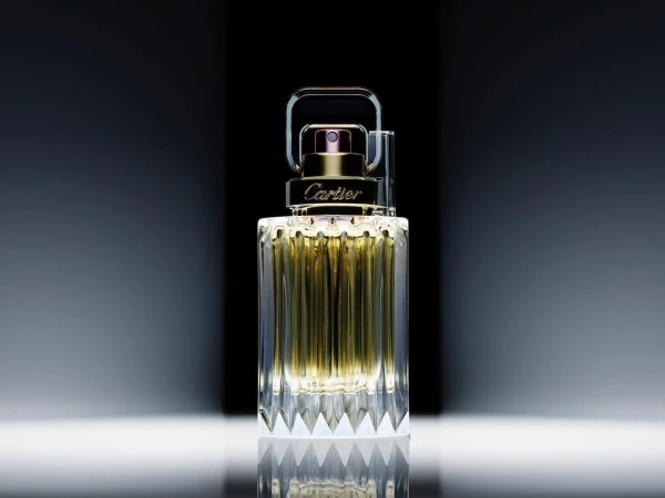 Elegant still life of Cartier fragrance bottle with gold accents and faceted glass design on a reflective surface, captured in studio lighting.