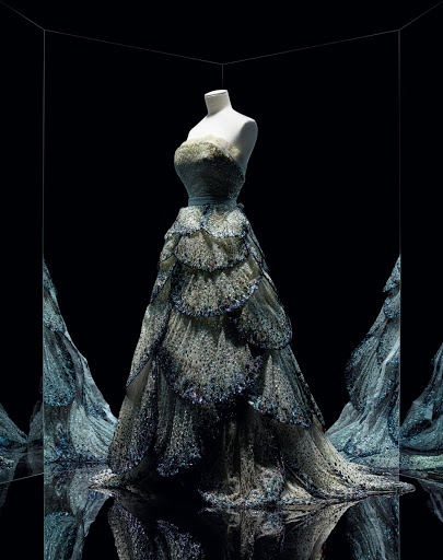 Elegant strapless evening gown with tiered skirt displayed on a mannequin in a mirrored room, fashion, and formal wear concept.