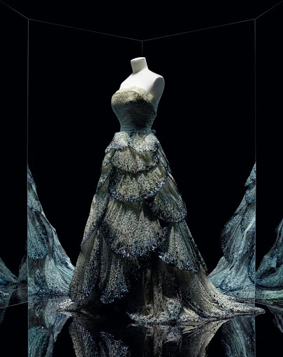 Elegant strapless evening gown with tiered skirt displayed on a mannequin in a mirrored room, fashion, and formal wear concept.