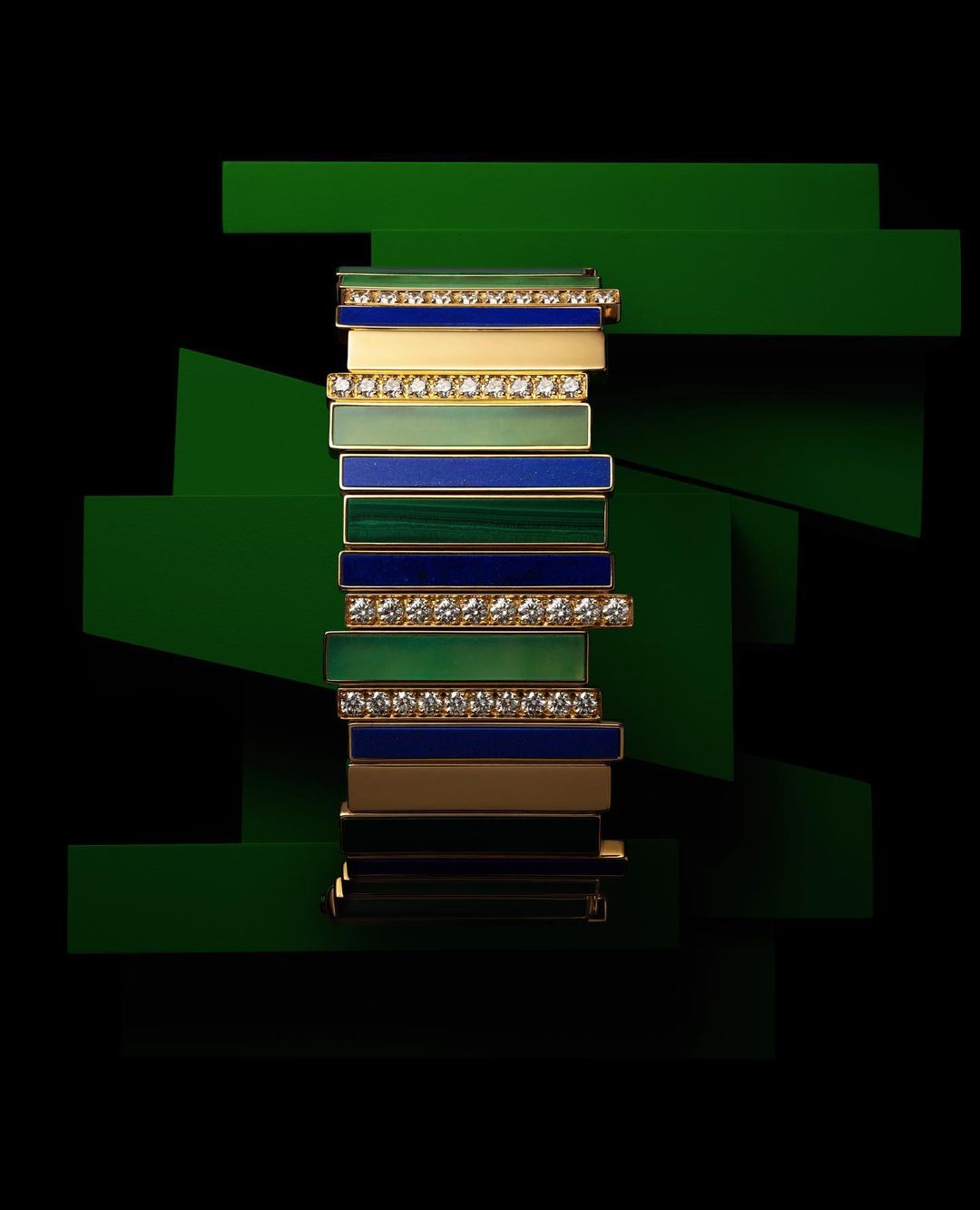 Stacked luxury gold bracelet with diamonds and colored enamel against a geometric dark green background. Jewellery fashion shot.