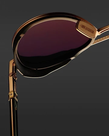 Close-up product shot showcasing the design and details of gold-rimmed sunglasses with purple lenses on a dark grey backdrop.