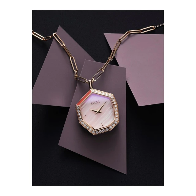 Elegant Dior watch pendant necklace with diamond bezel and chain, displayed against geometric lilac and black panels in a studio shot.