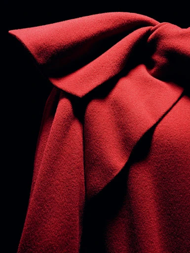 Close-up of textured dark red fabric draped with overlapping layers and shadows against a stark black background, showcasing texture and color.