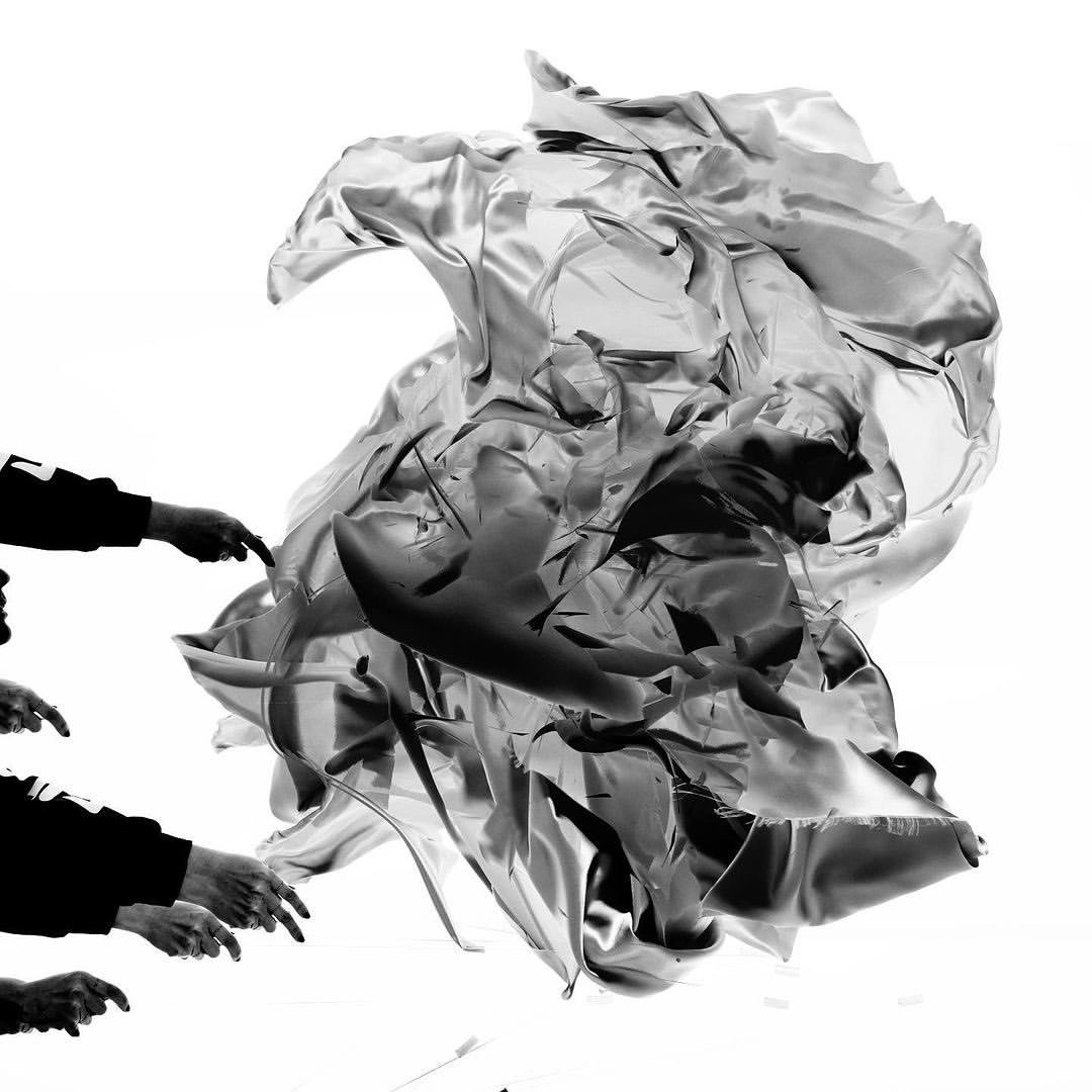 Monochrome image showcasing multiple hands interacting with shiny, crumpled fabric against a bright white backdrop, creating a dynamic composition.