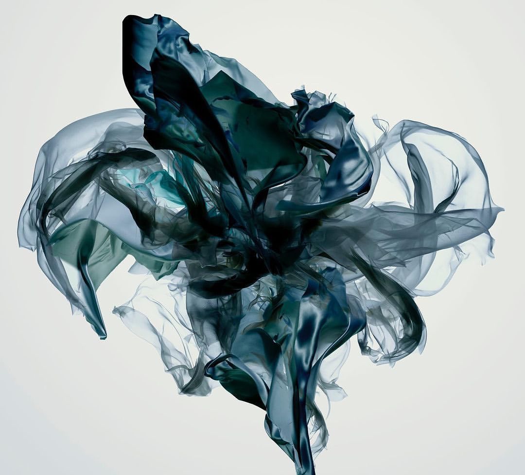 Dynamic composition of suspended dark blue and green sheer fabric swirling against a white background