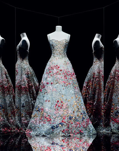 Elegant floral gown on a mannequin, surrounded by multiple reflections in a dark studio setting. Couture fashion design showcase.