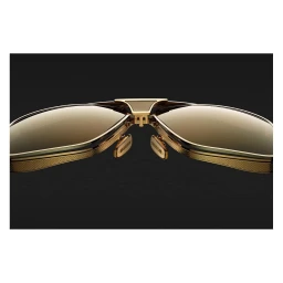 Extreme close-up product shot of luxury gold aviator sunglasses featuring detailed textured metal frames against a dark background.