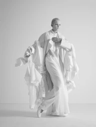 Monochrome portrait of a model in voluminous white layered garments posing against a seamless background