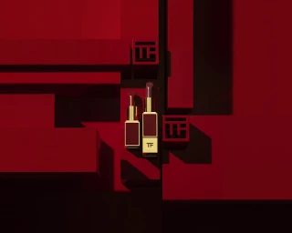 Two Tom Ford lipstick tubes standing vertically among deep red geometric architectural blocks under directional studio light.