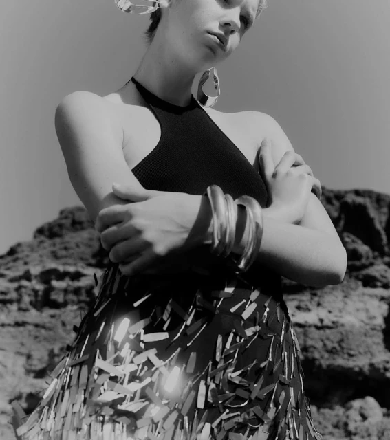 Black and white studio shot featuring a stylish adult female model wearing oversized hoop earrings, metal cuff bracelets, and an embellished skirt.